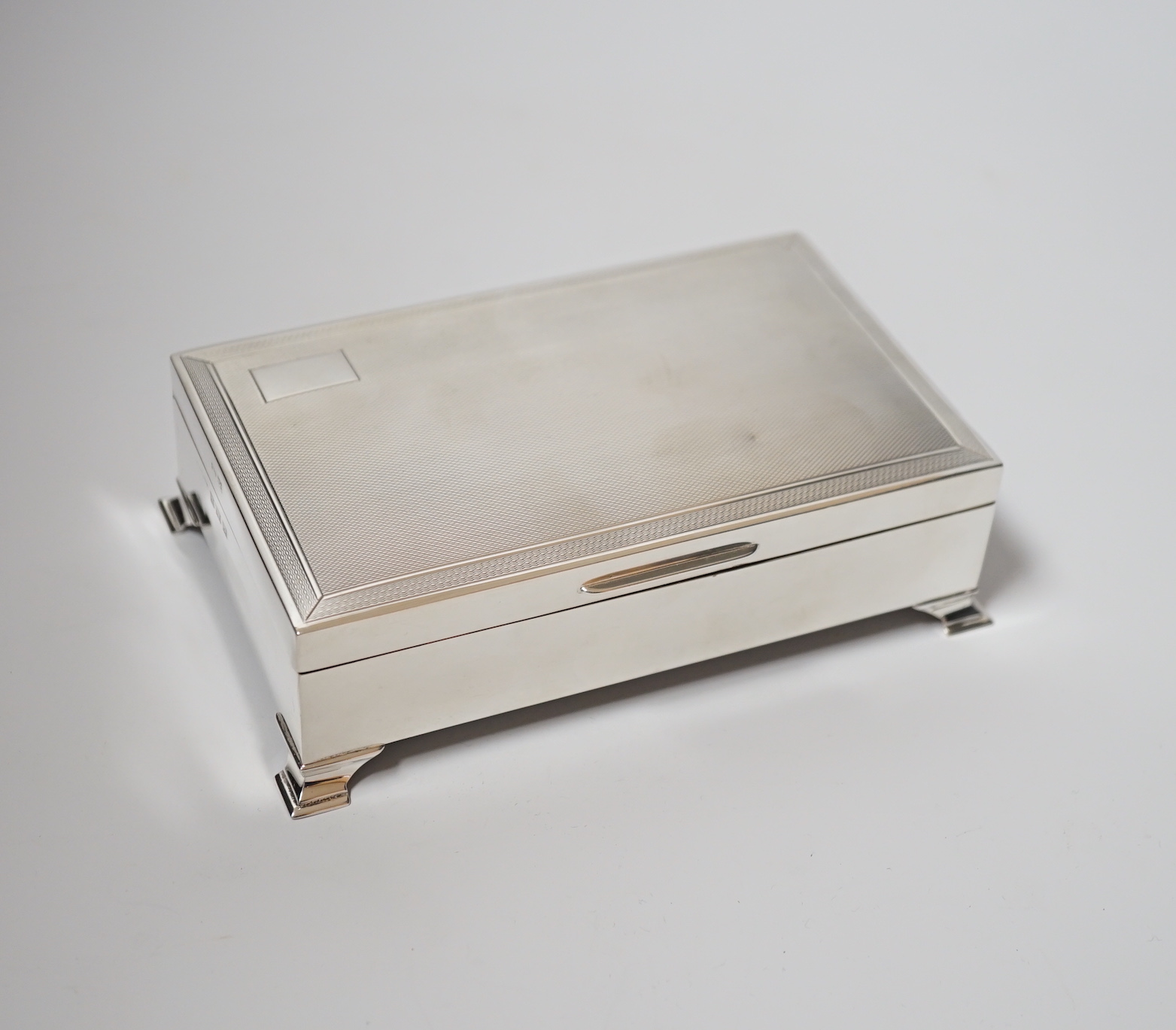 An Elizabeth II engine turned silver mounted rectangular cigarette box, Birmingham, 1961, 15.4cm, on bracket feet.